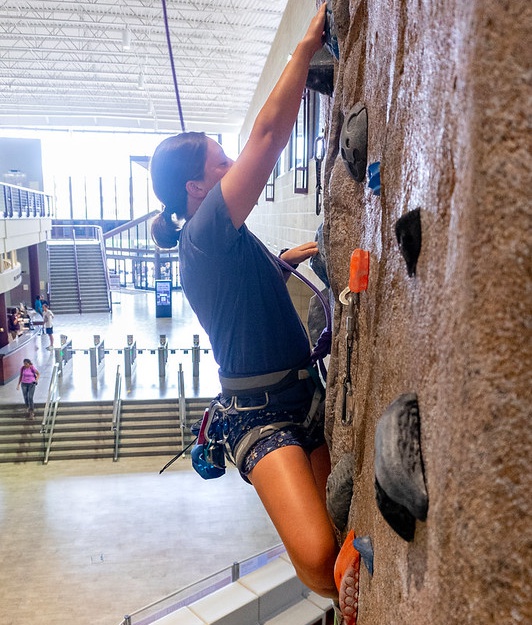 A student is climbing on the Rockwall in the Student Rec Center.