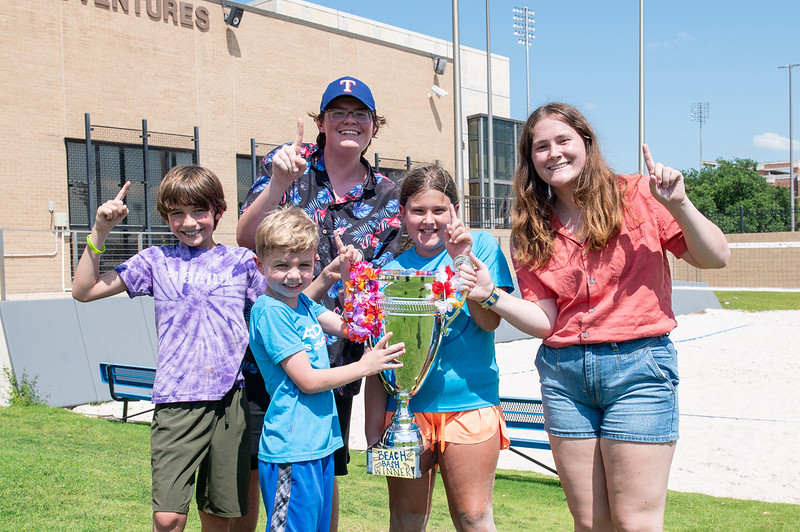 Two counselors standing with 3 children celebrating their win with a a trophy in hand.