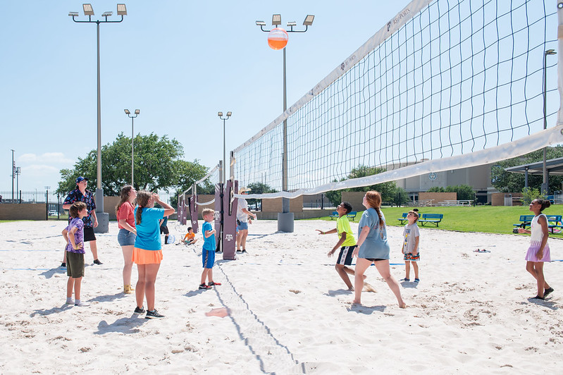 Kids and counselors are playing sand volleyball outside at the Rec backyard.