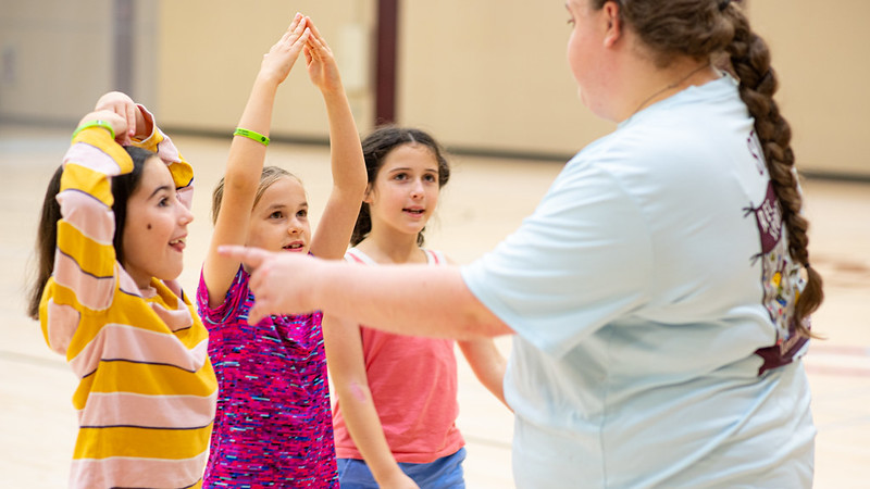 Female counselor is explaining instructions to the game to three children.