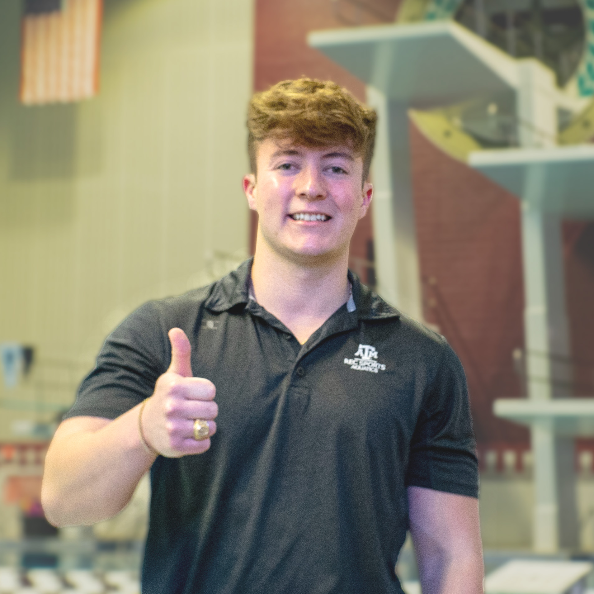 Ciaran is standing in front of the dive well in the Student Rec Center smiling and giving a thumbs up.