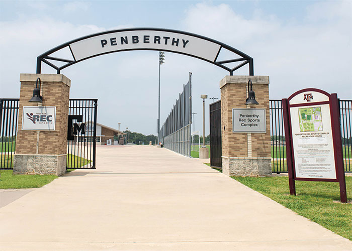 A gate to a baseball field with a sign that says penberthy. A gate to the outdoor turf and grass fields with a sign that says Penberthy Rec Sports Complex.