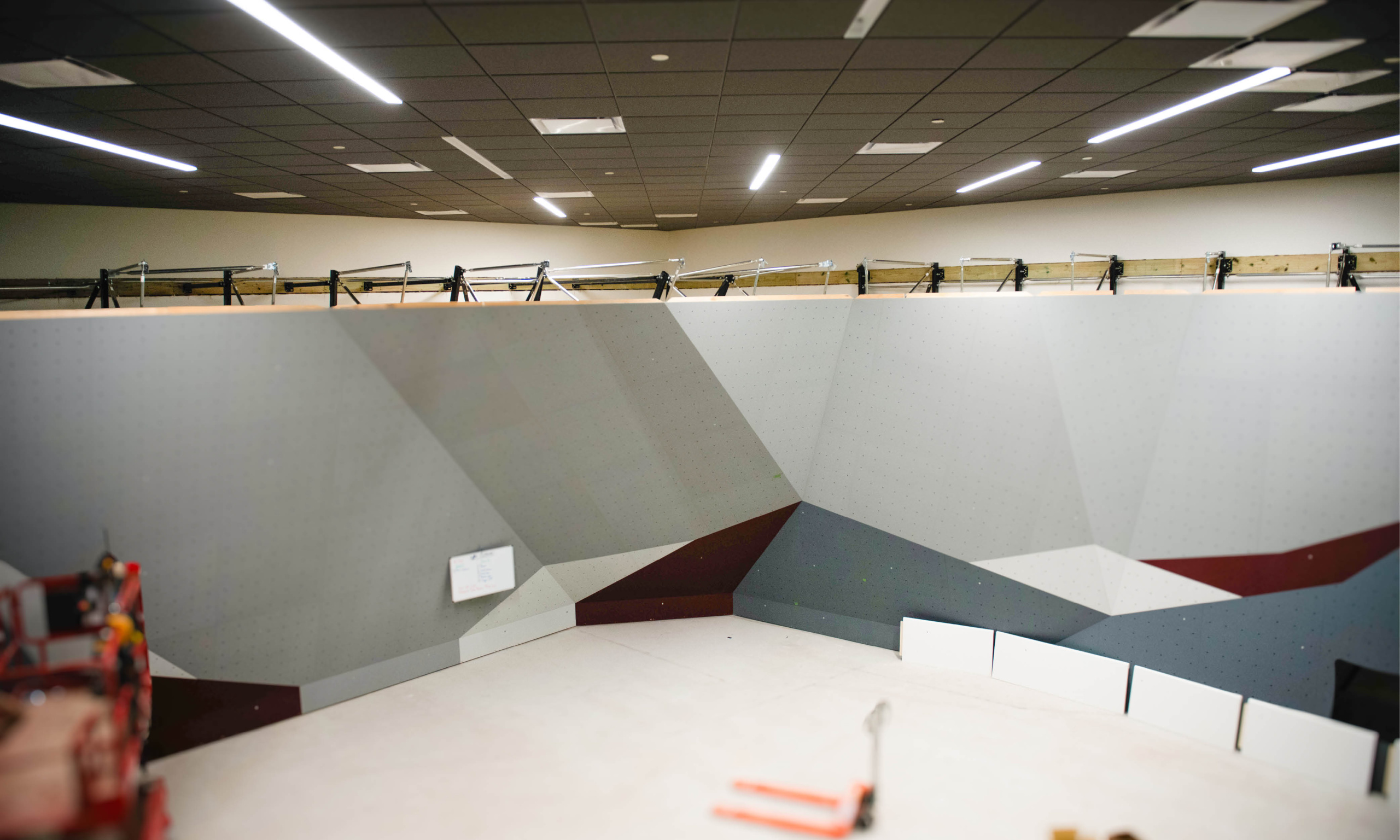 Wide view of the new indoor bouldering wall at Texas A&M Rec Sports under construction, with geometric gray and maroon panels.