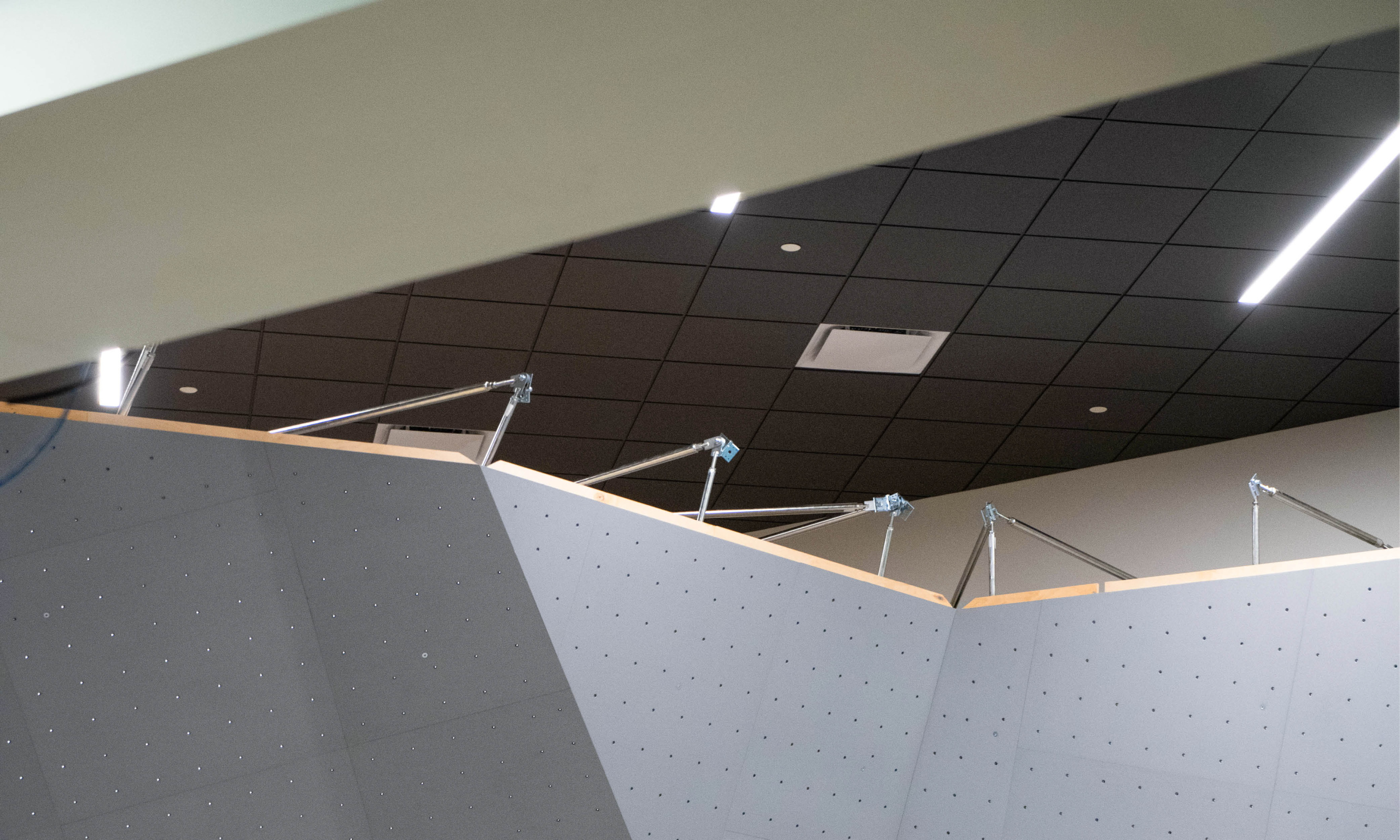 Close-up of the upper section of the bouldering wall under construction, showing support beams and lighting above.