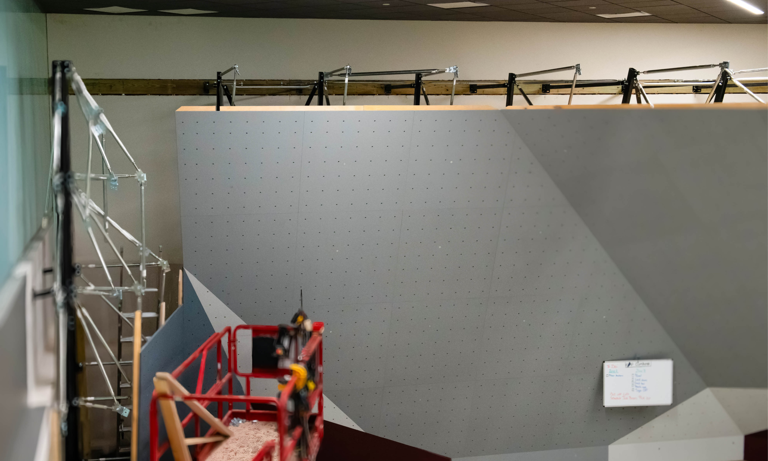 Side view of the bouldering wall under construction with scaffolding and a red lift visible.