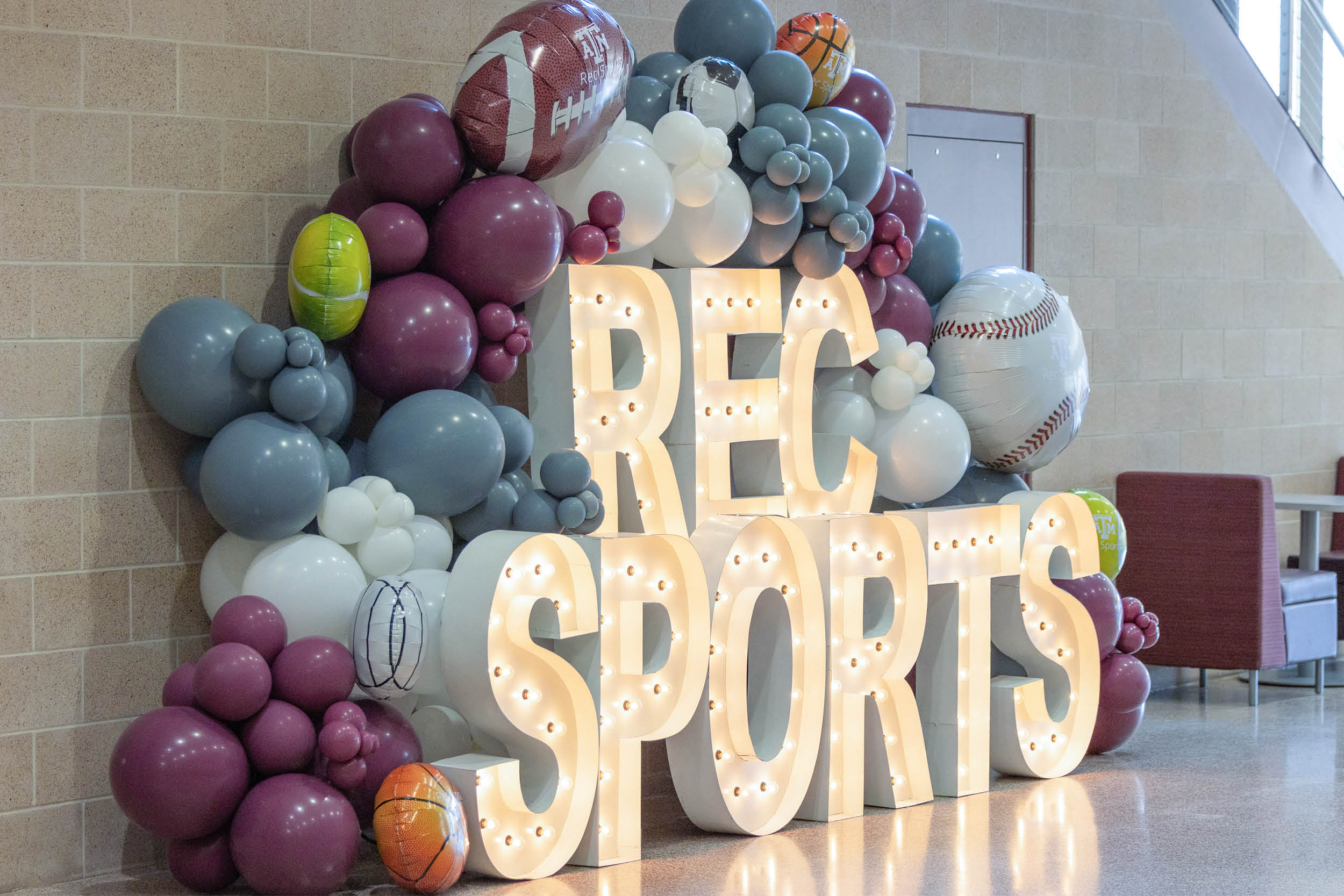 Large illuminated “REC SPORTS” letters surrounded by maroon, white and gray balloon décor inside the Student Rec Center.