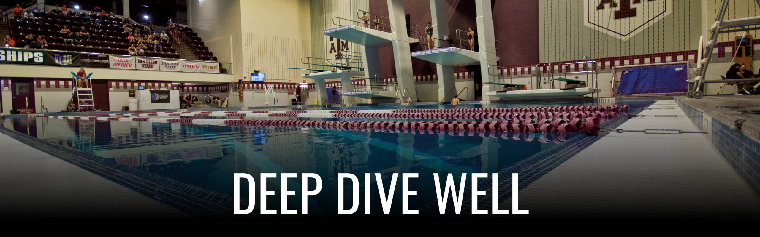 Interior of the Texas A&M University swimming pool featuring the 'DEEP DIVE WELL' sign, with clear blue water and lane markers visible.