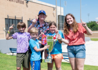 Children and counselors smiling and holding a large trophy labeled “Beach Bash Winner” outside the Rec Sports facility.