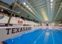 Indoor swimming pool at Texas A&M University with maroon signage and diving platforms reflected in the water.