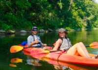 Two students kayaking on a calm river surrounded by trees during an Outdoor Adventures trip.