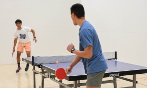 Two men playing ping pong on a racquetball court in the Student Rec Center.