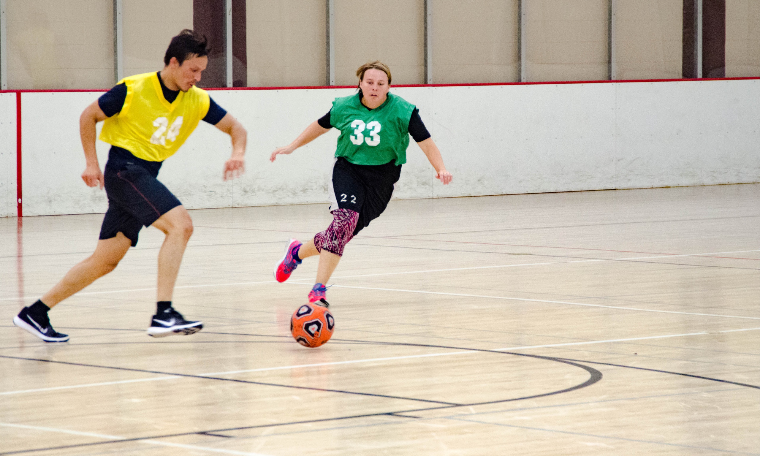 A pair of individuals actively participating in an intramural coed soccer match on a court, showcasing their passion for the game.