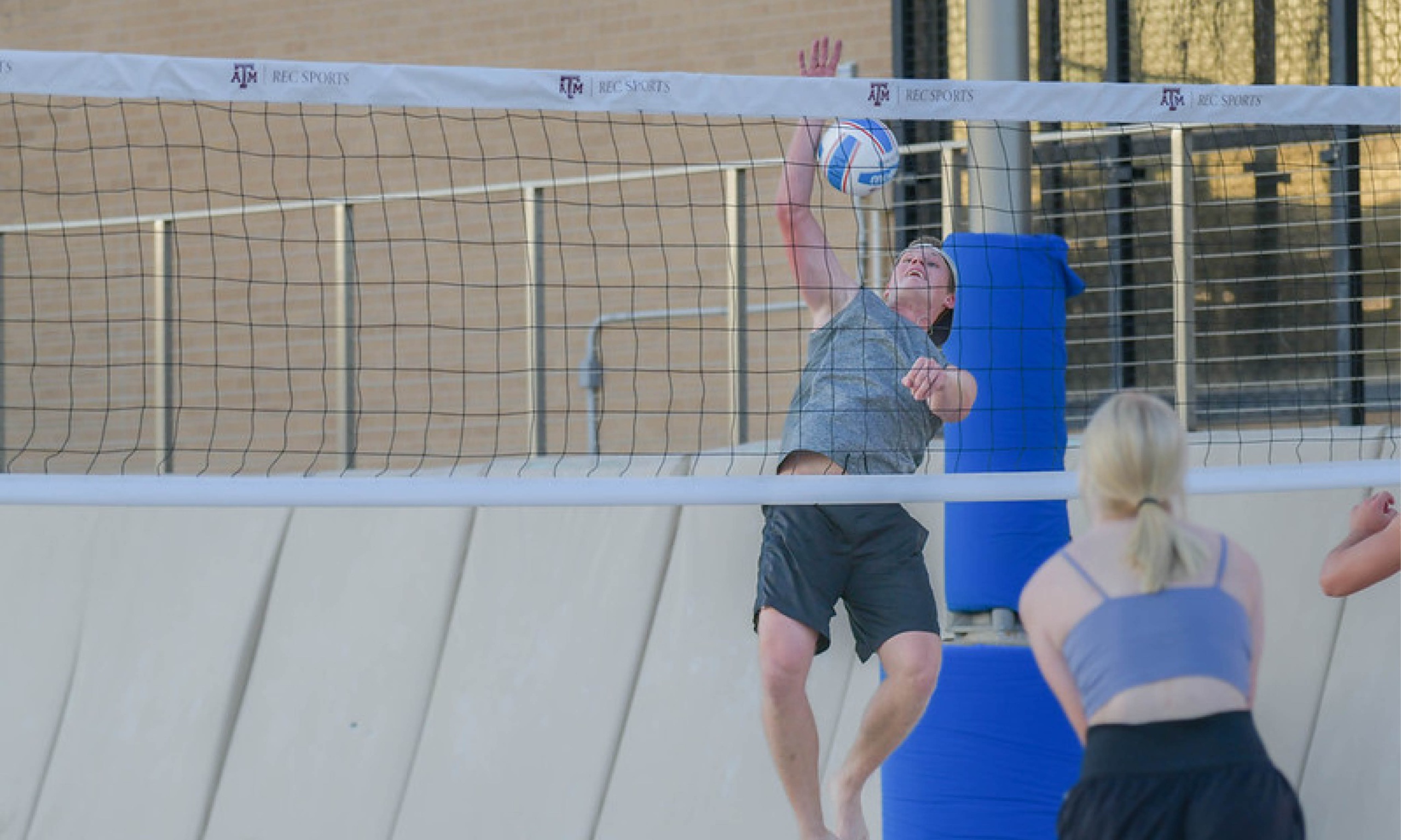 Guy hitting a volleyball over the net to a female out on the san volleyball courts at the Student Rec Center.