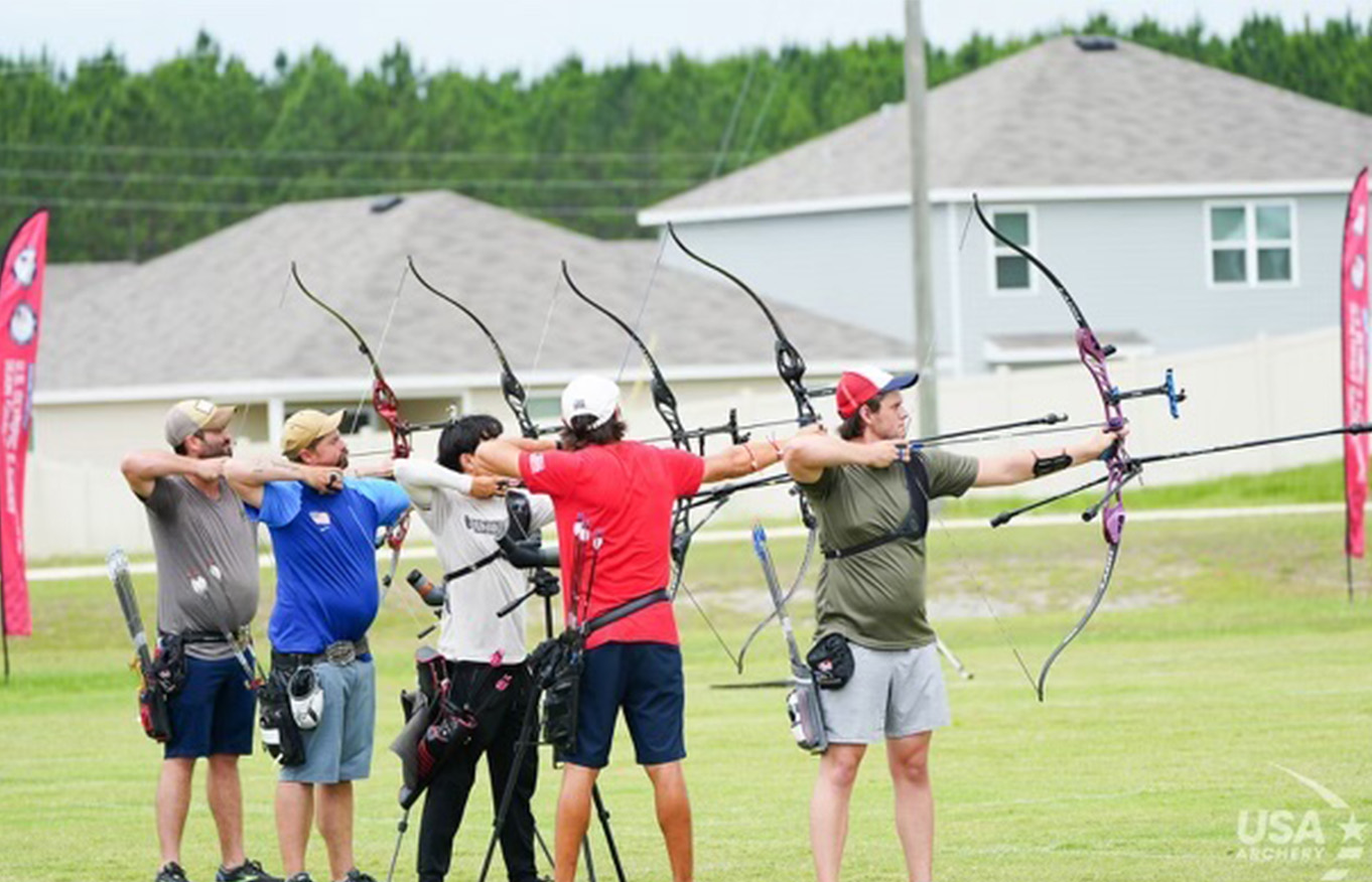 Men stand side by side, holding up their bows and competing in the USA Archery Olympic trials.