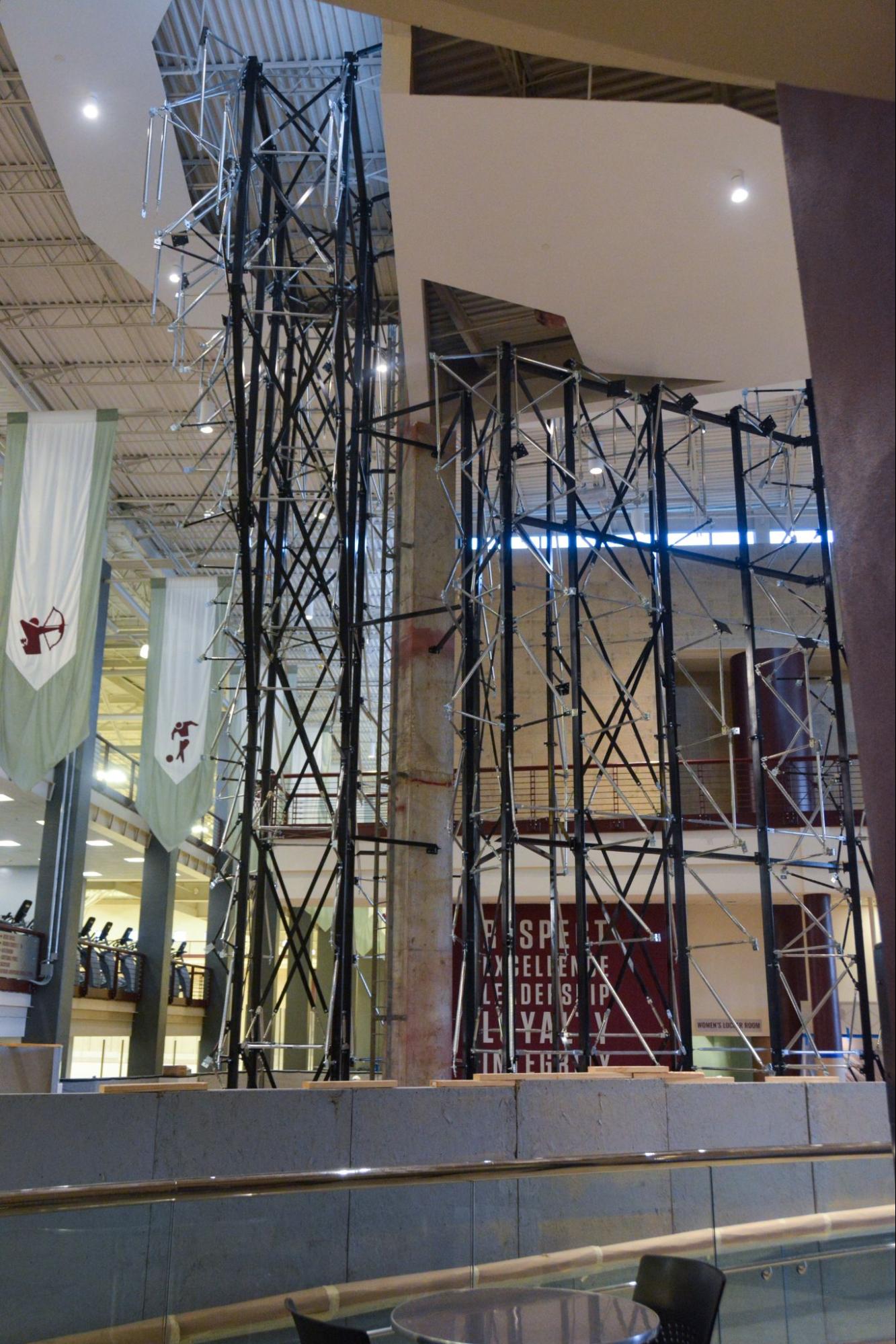 Tall black metal climbing wall frames rising multiple stories inside the Student Rec Center lobby, surrounded by open atrium space and hanging banners.