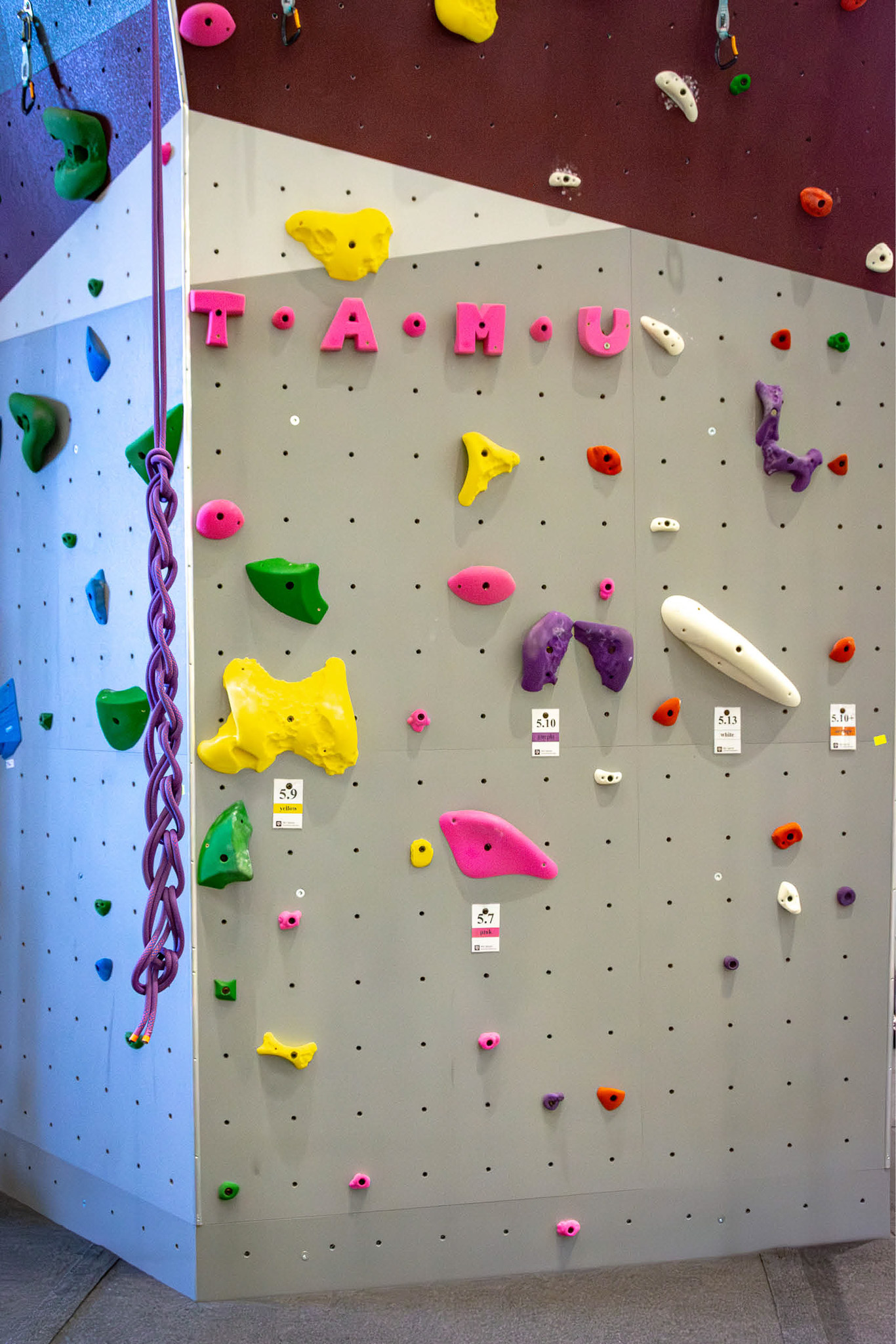 Close-up of the indoor climbing tower at Texas A&M Rec Sports, showing colorful routes and maroon-and-gray wall patterns.