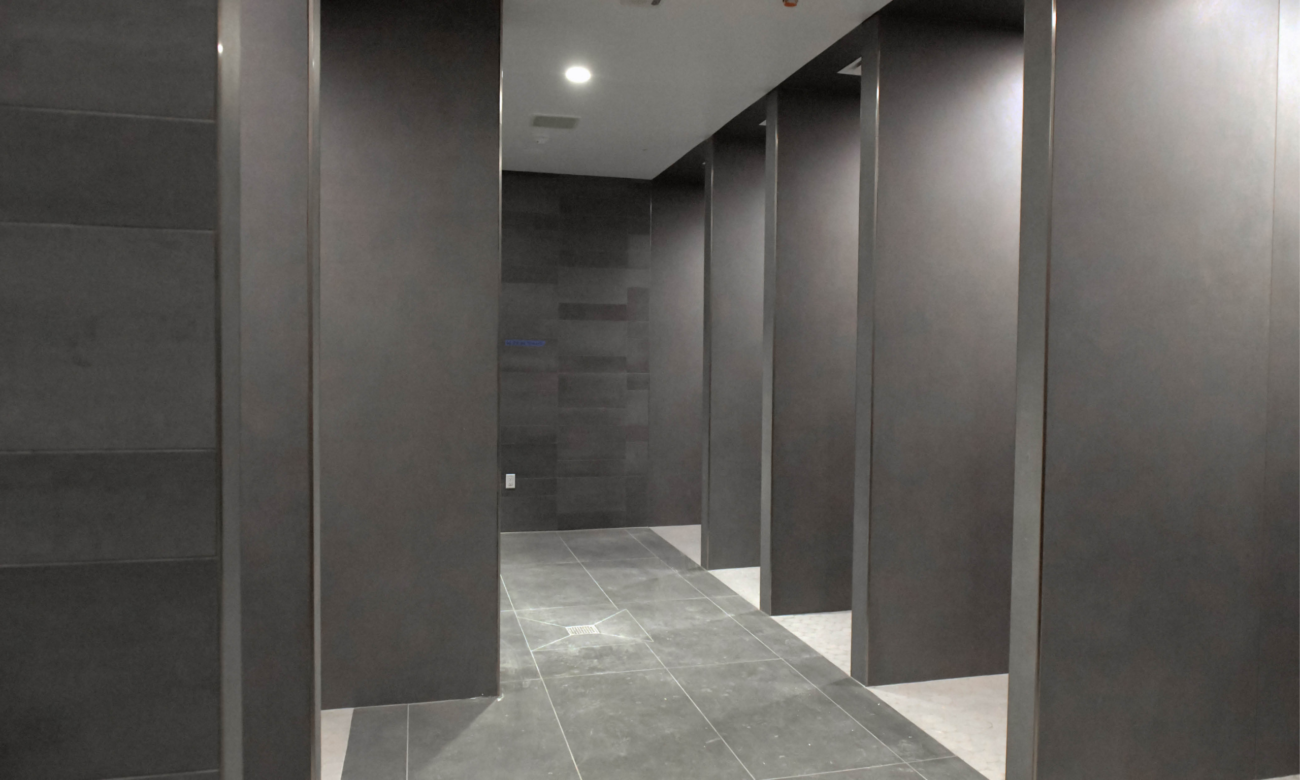 Wide hallway of shower stalls with dark tile in the renovated locker room.