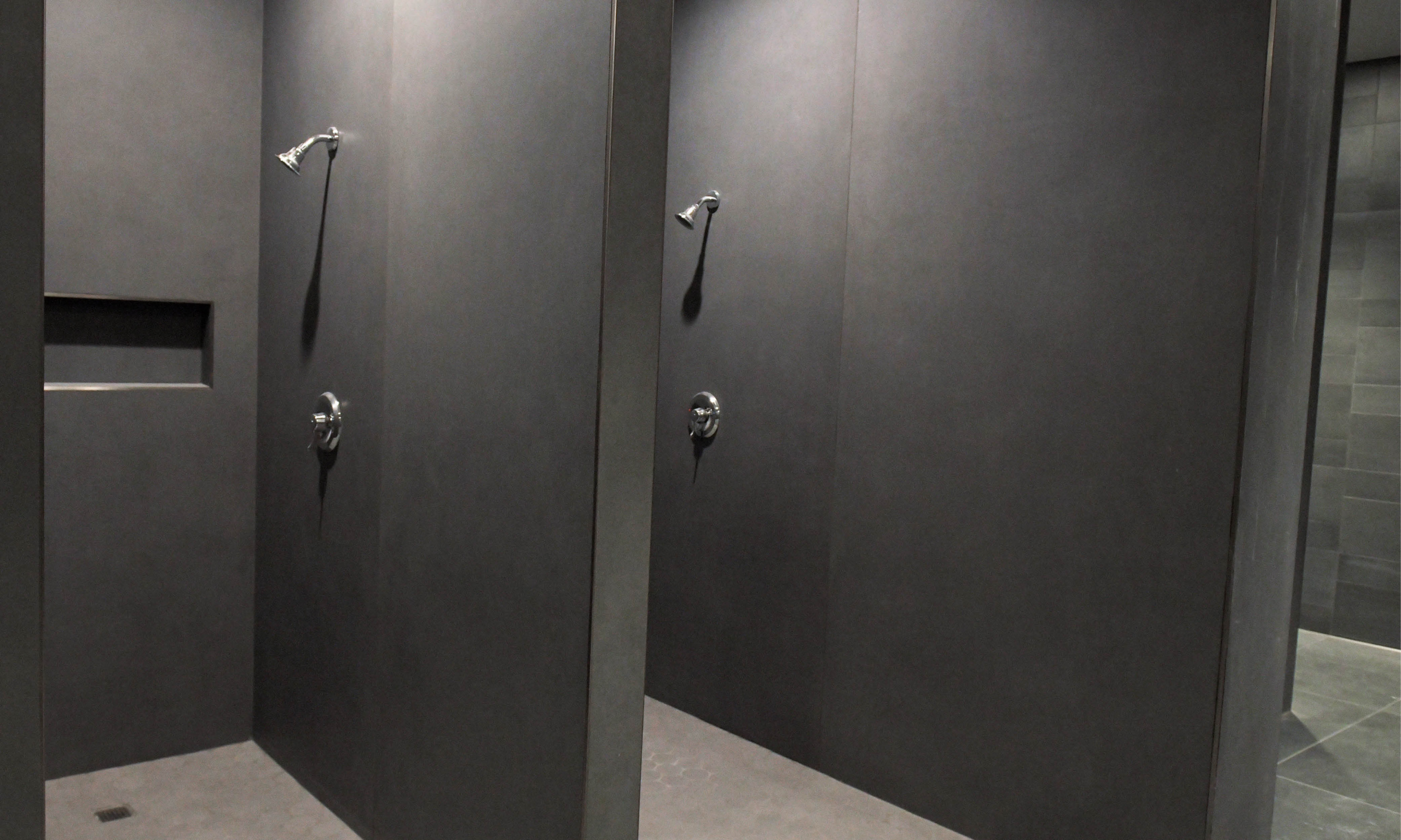 Dark-tiled shower stalls with overhead showerheads in the renovated locker room.