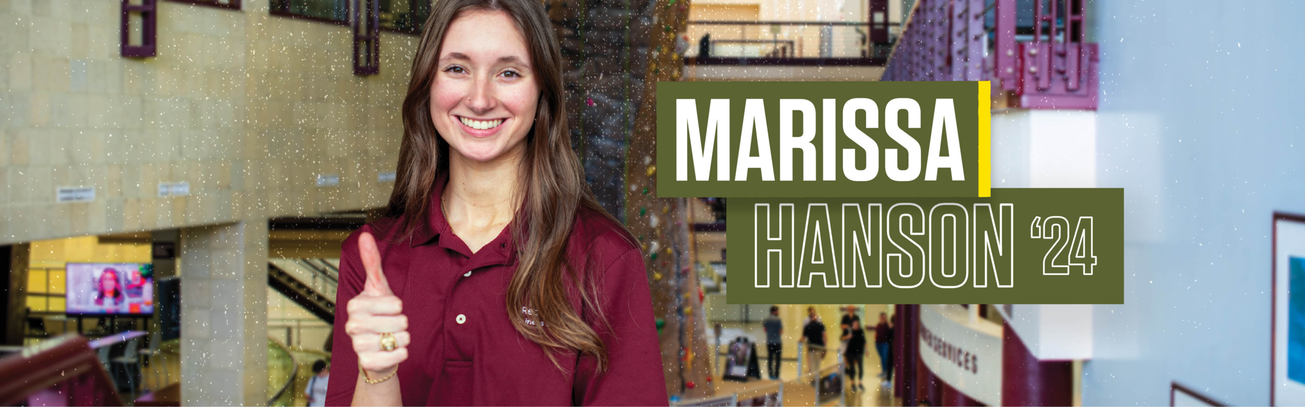 Marissa Hanson is standing inside the student rec center with the indoor climbing facility behind her giving a thumbs up.