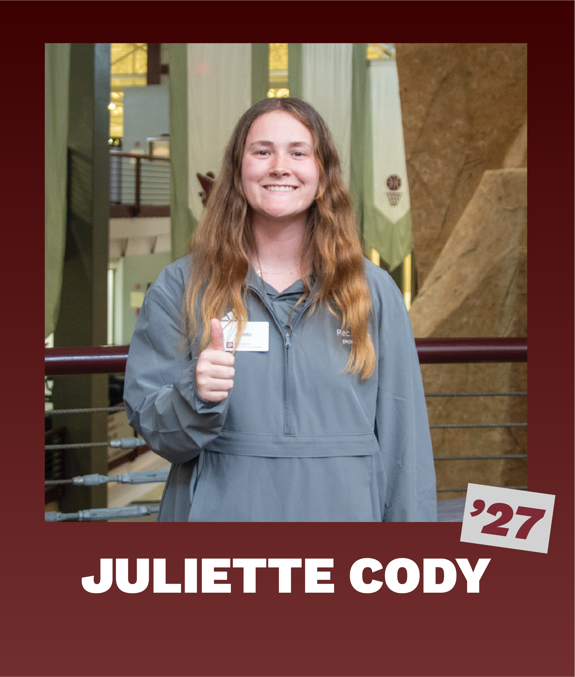 Juliette Cody, wearing a gray polo Rec Sports pullover, smiling with a thumbs up, standing inside the Student Rec Center with banners in the background.