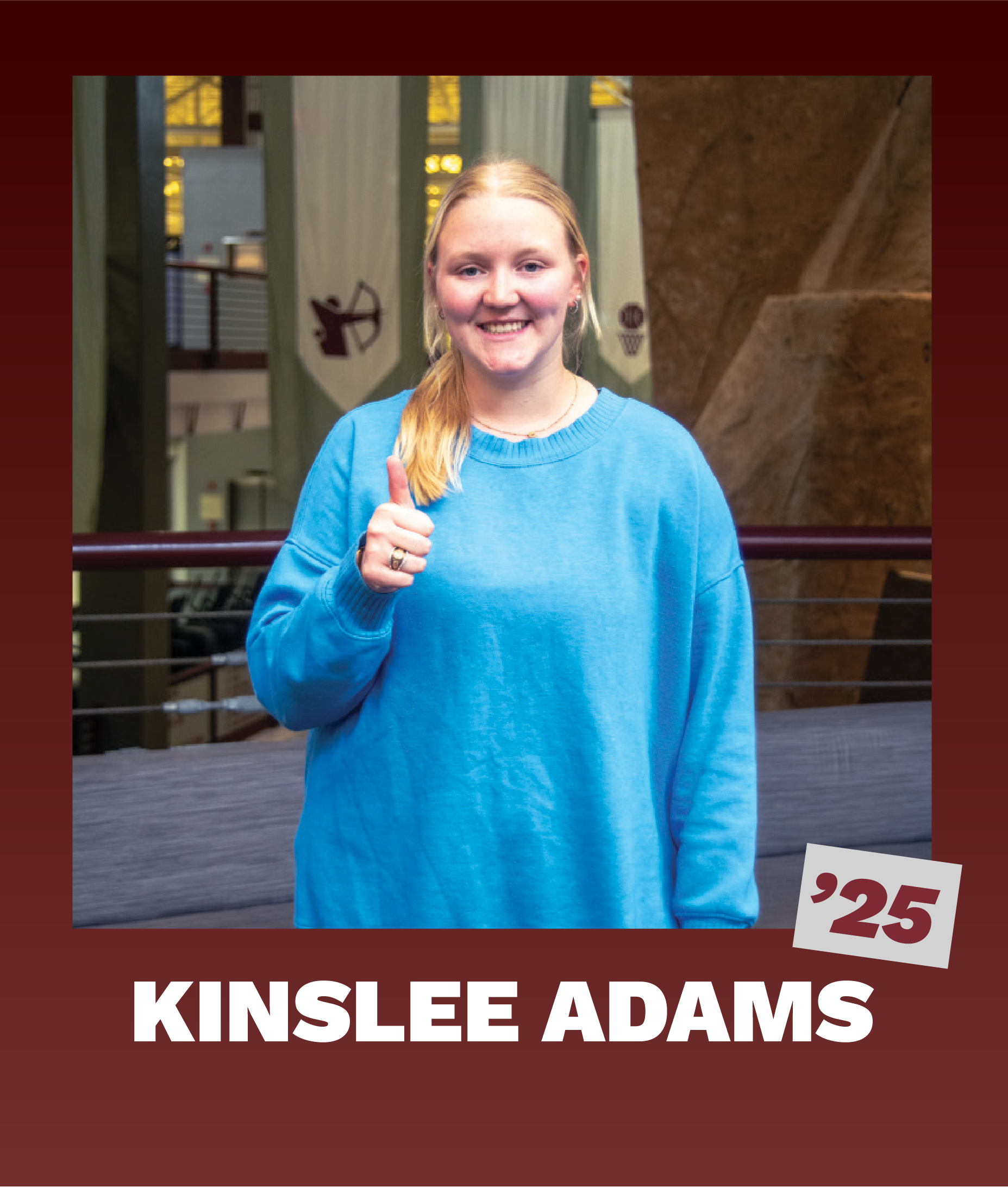 Kinslee Adams, class of '25, smiling and holding a thumbs up inside the Student Rec Center with banners and rockwall in the background