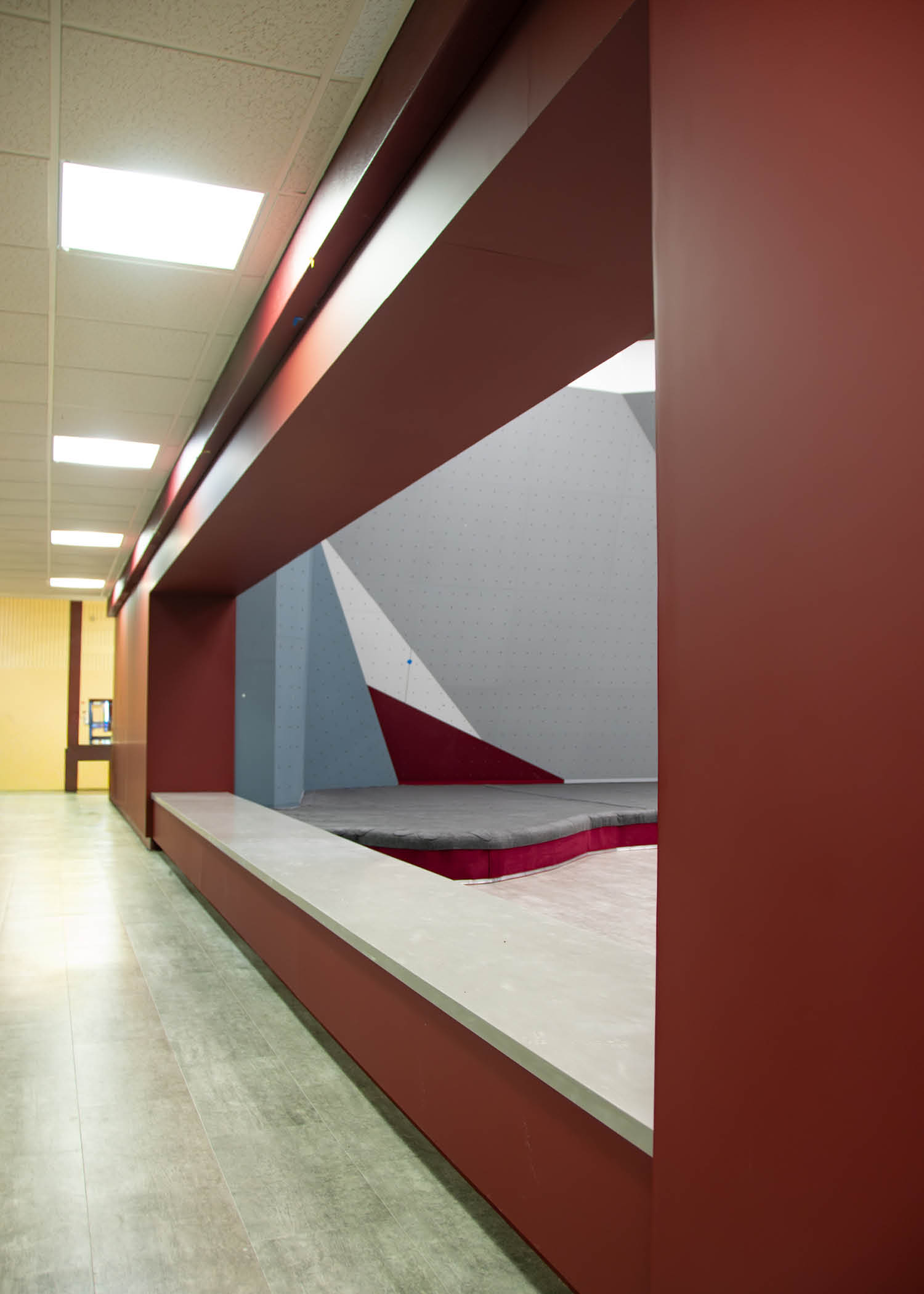 View from the hallway showing the entrance to the new bouldering area framed by maroon walls and modern lighting.