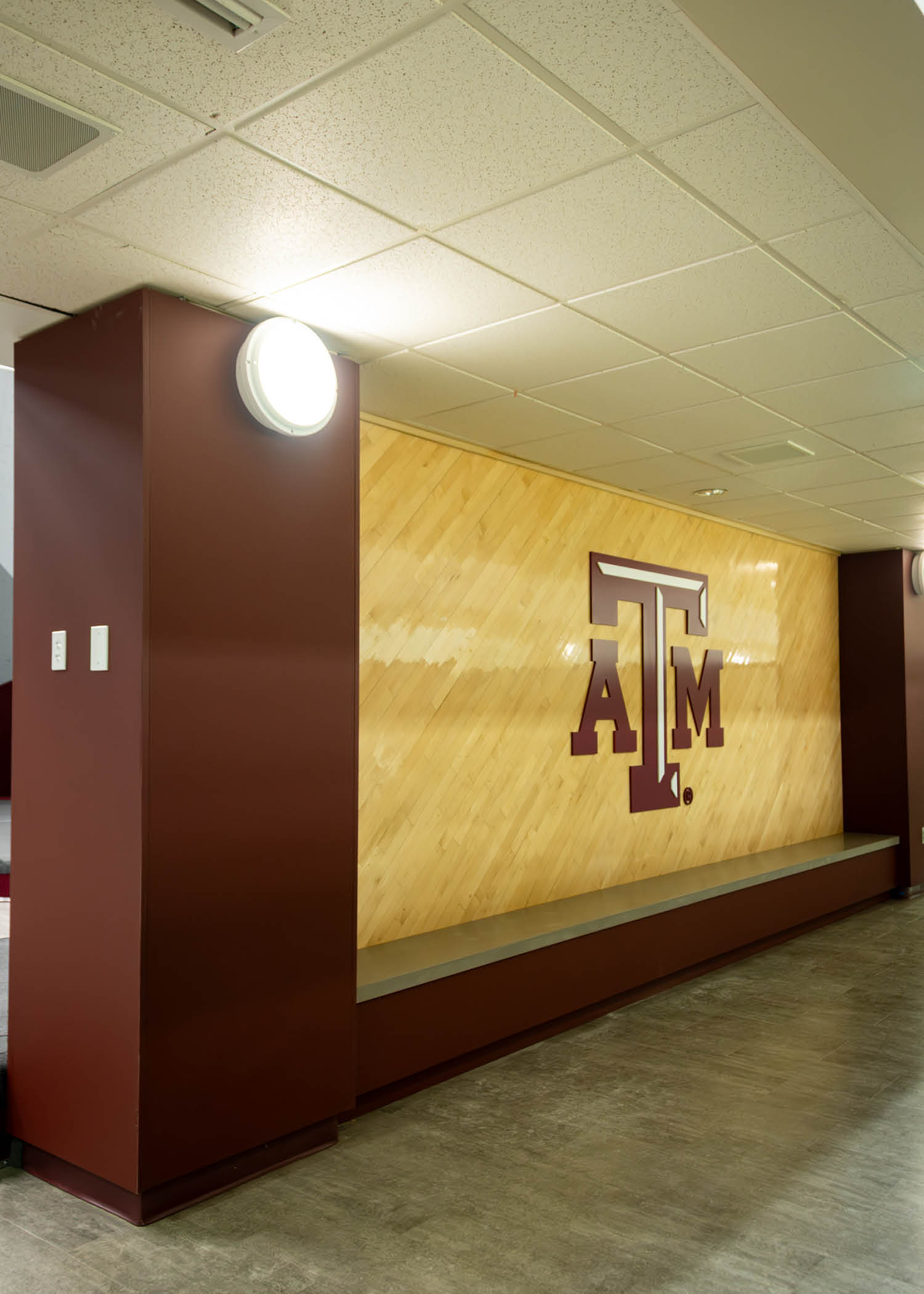 Renovated hallway outside the bouldering space featuring a large maroon Texas A&M logo set against wood paneling.
