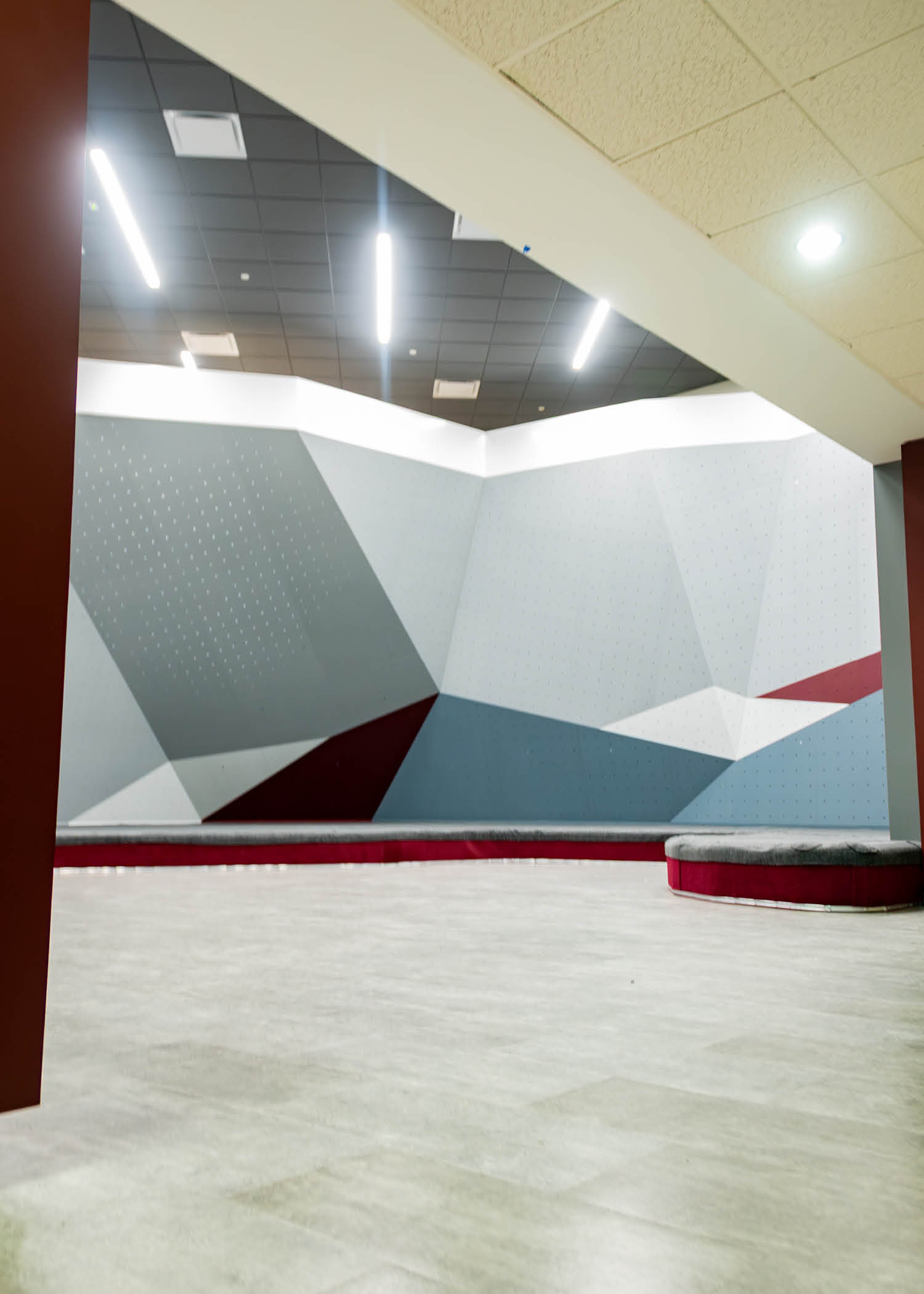 Close-up of the bouldering wall design with red, white, and gray angled panels and soft padding below.