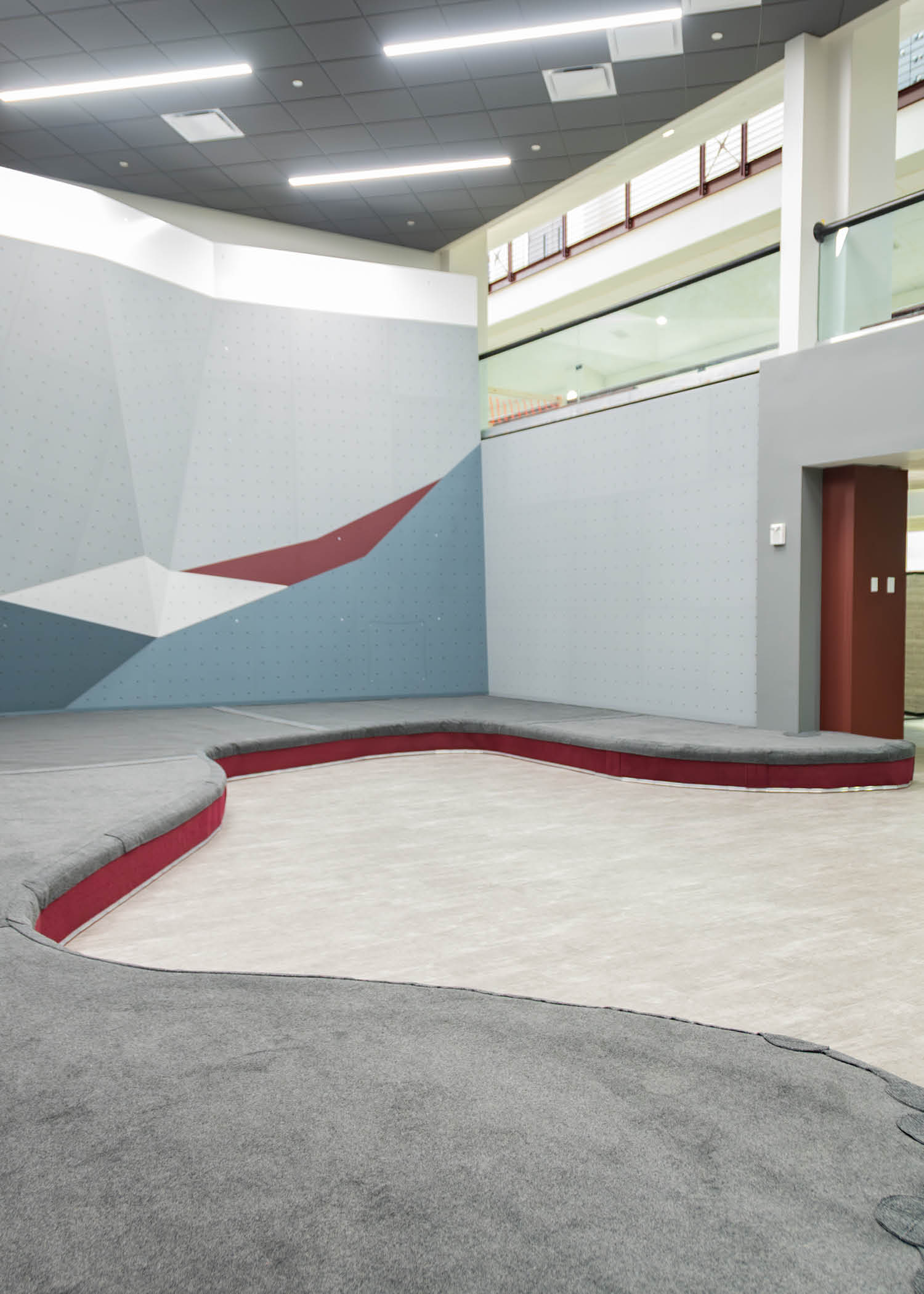 Wide view of the bouldering space from the entryway, highlighting new wall angles and gray floor padding.