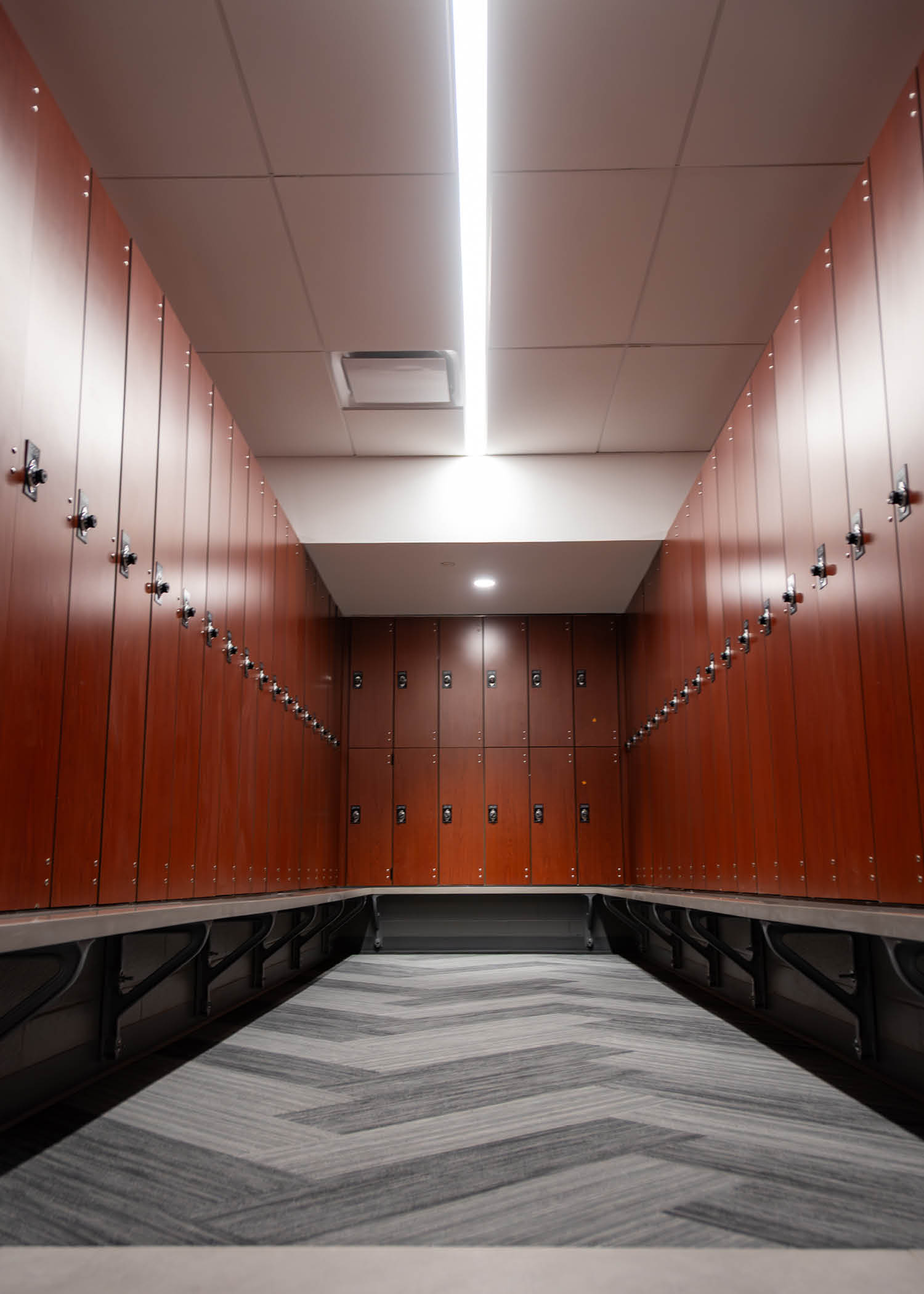 Sleek locker room with rows of wood-finish lockers, gray herringbone flooring, and overhead LED lighting.