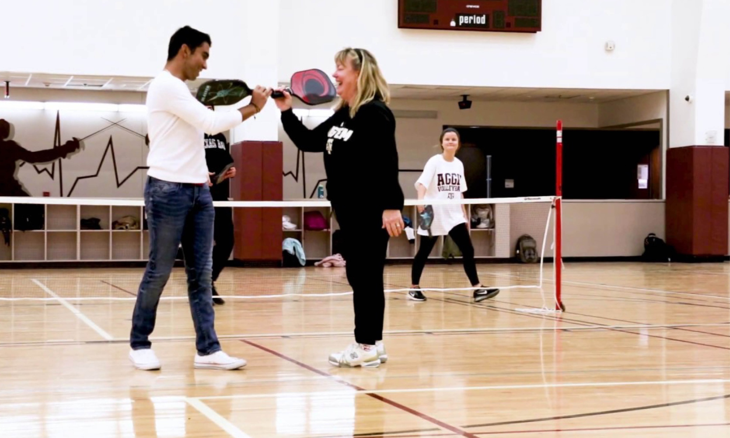 Two people playing badminton in a gym.