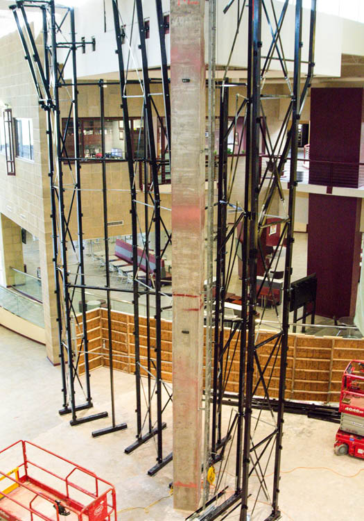 Interior view of a construction site with scaffolding and a tall concrete pillar, overlooking the staff offices.