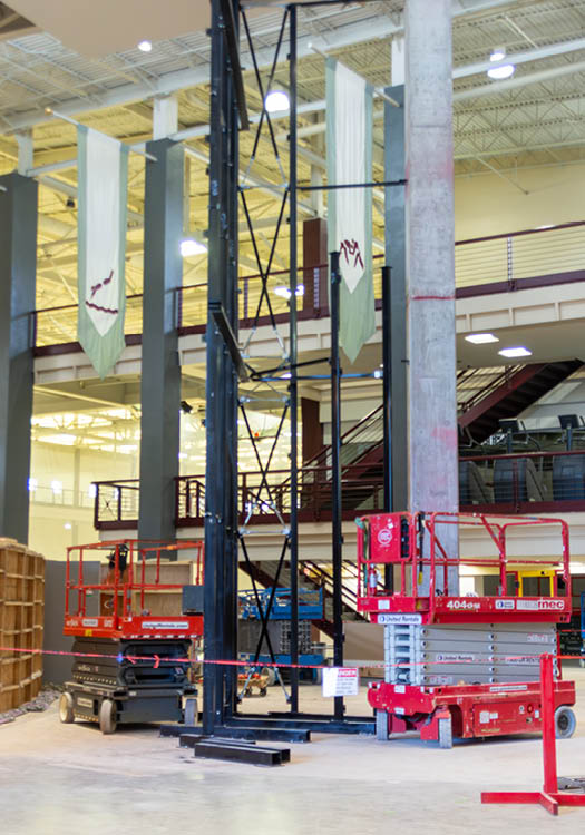 Construction scaffolding inside a building with an aerial work platform and tools visible on the ground floor the 2nd and 3rd floor and courts 1-4 in the background.