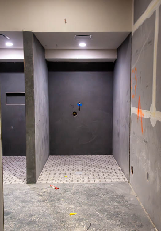Interior of an unfinished shower with grey walls and white tiled flooring.