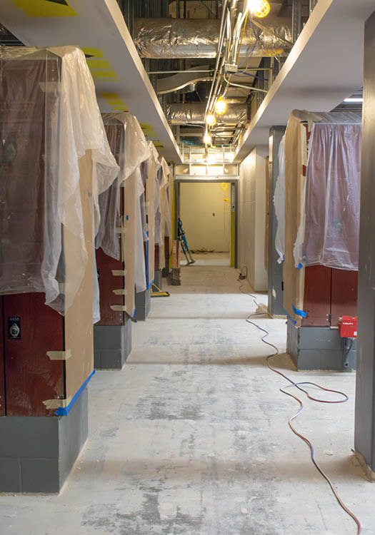 Interior view of a hallway under construction, featuring exposed ceiling ducts, covered lockers, and construction tools.