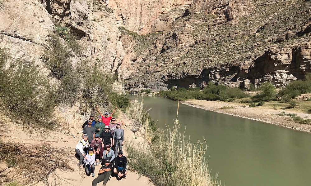 Group of people posing in front of a river with cliffs in the background, likely at a national park or natural reserve.