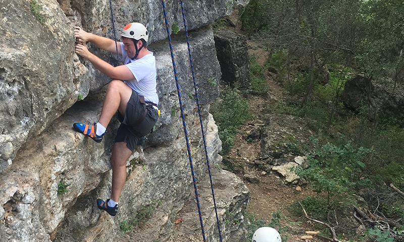 Student Climbing a rockwall outside with support from fellow climbers.