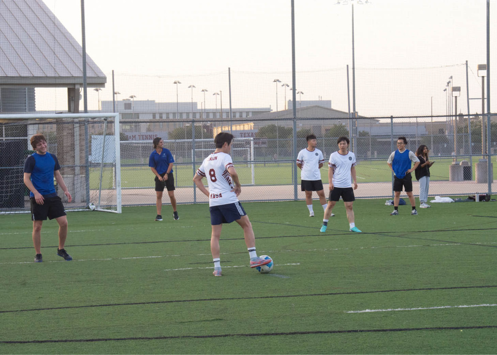 Sports_soccer Group of people playing soccer on an outdoor field, with one individual preparing to kick the ball.
