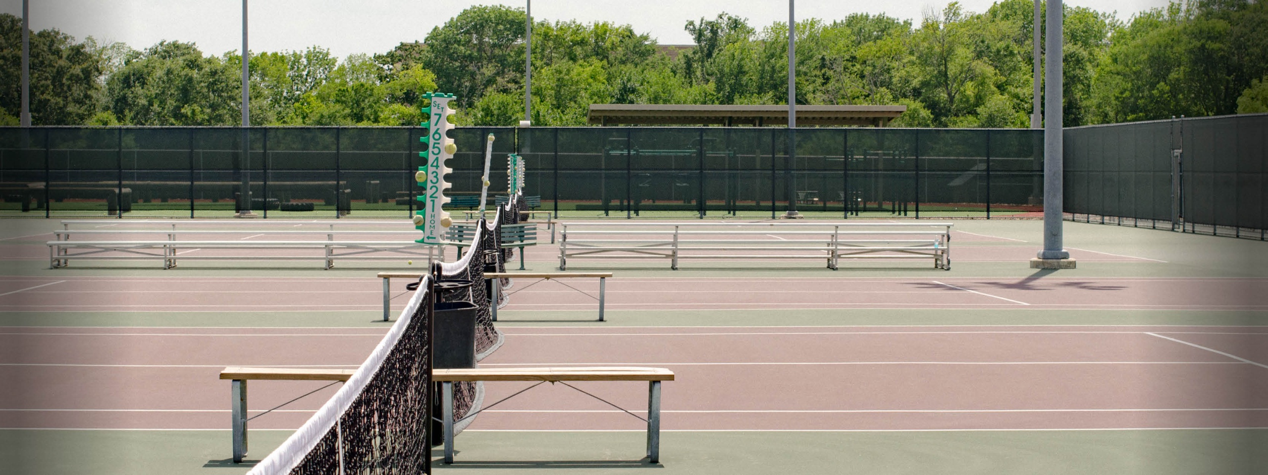 Outdoor tennis court with seating and net.