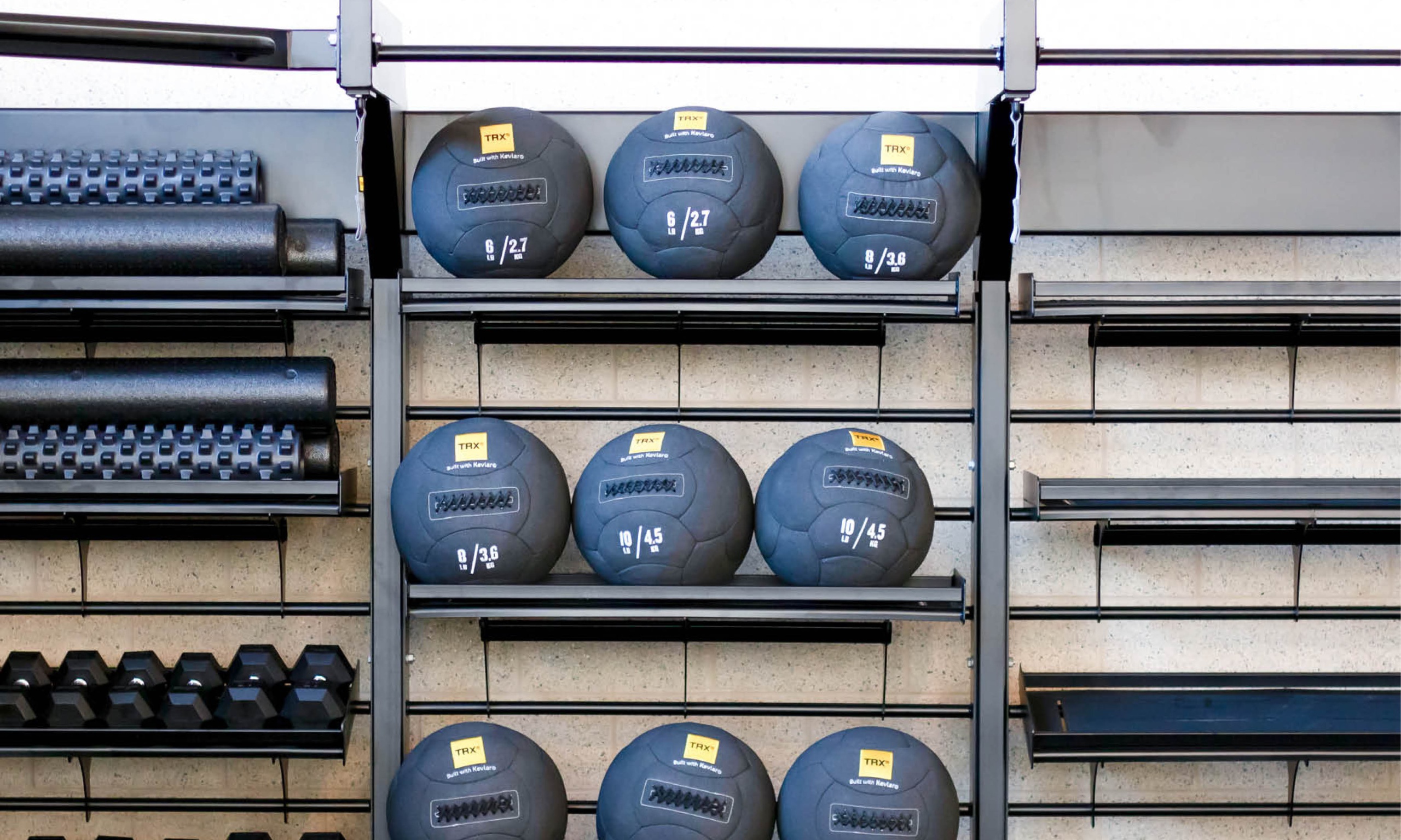 a display rack against the wall in the strength and conditioning room that includes medicine balls, free weights, and ropes.
