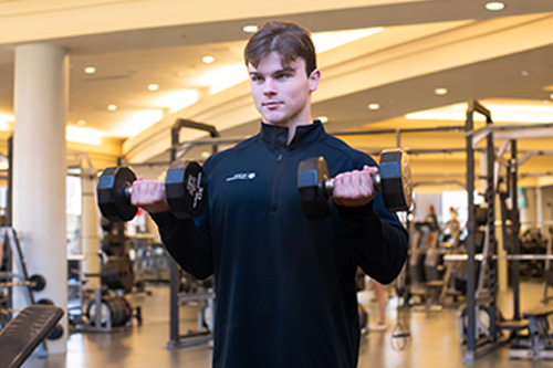 Strength & Conditioning room employee lifting dumbbells.