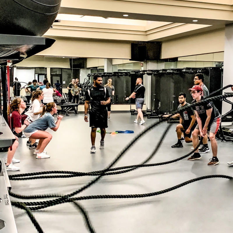 A group fitness class in a gym, featuring individuals participating in various exercises including rope workouts.