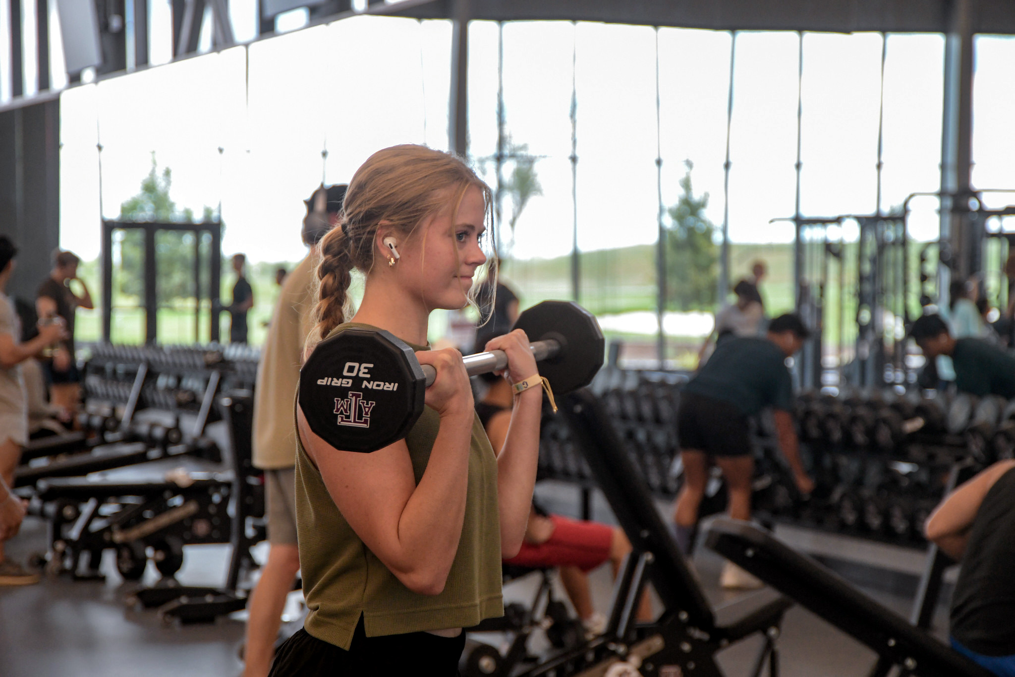 A student lifting dumbbells in the weight room, with the Texas A&M University logo visible on the equipment.