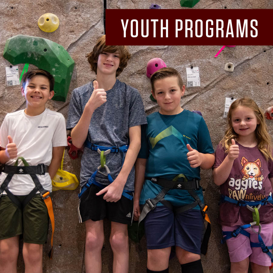 Four children are standing in front of the indoor climbing facility inside the Student Rec Center. In the top right corner of the image it says Youth Programs.