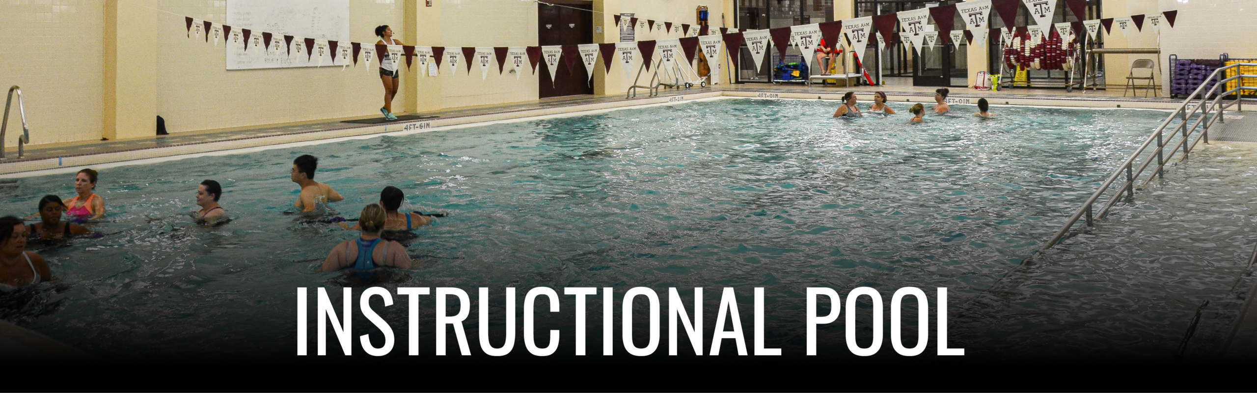 Group of people participating in a swimming class in an indoor instructional pool, with banners hanging above the water.